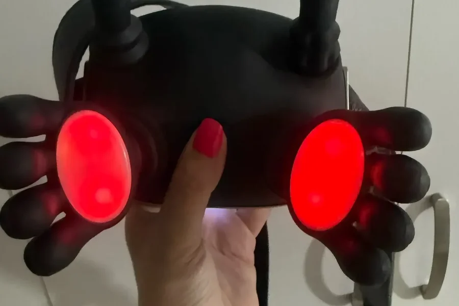 Das schwarze Massagegerät in zwei Händen gehalten, die beiden Wärmepads in den Handflächen leuchten rot